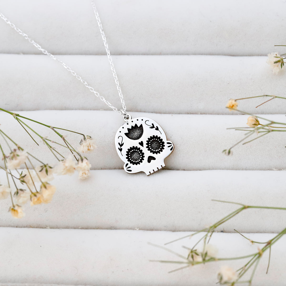 Skull-shaped pendant necklace on a white surface with small flowers