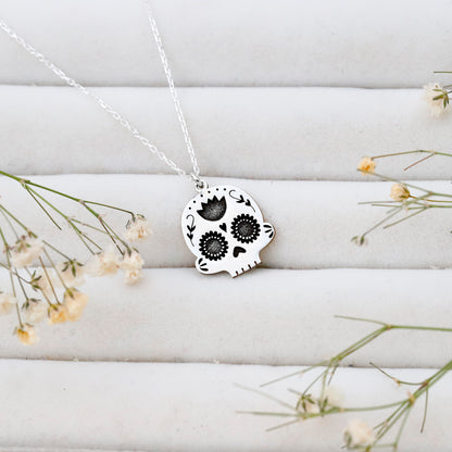 Skull-shaped pendant necklace on a white surface with small flowers