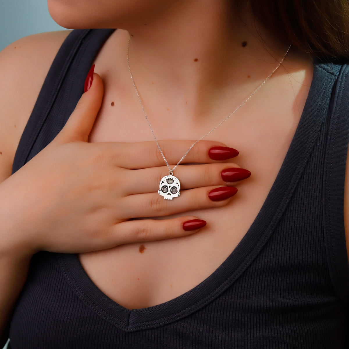 Person wearing a silver necklace with a skull pendant, hand on chest.