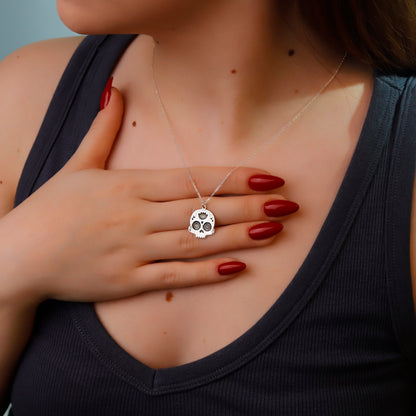 Person wearing a silver necklace with a skull pendant, hand on chest.