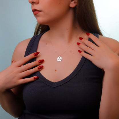 Woman wearing a necklace with a clover pendant against a neutral background