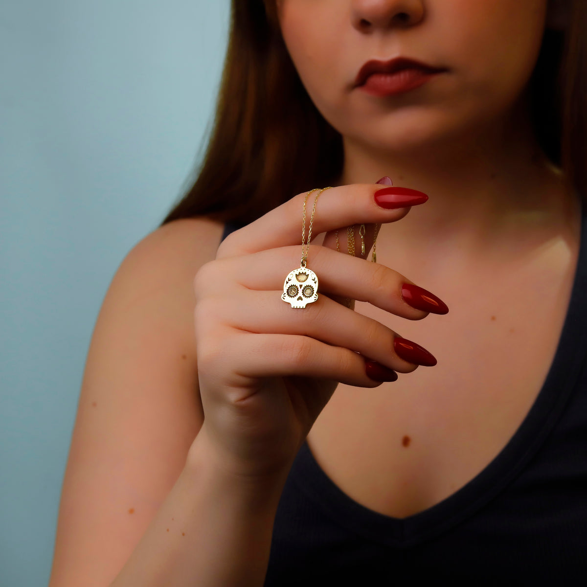 Woman holding a gold necklace with a skull pendant against a blue background