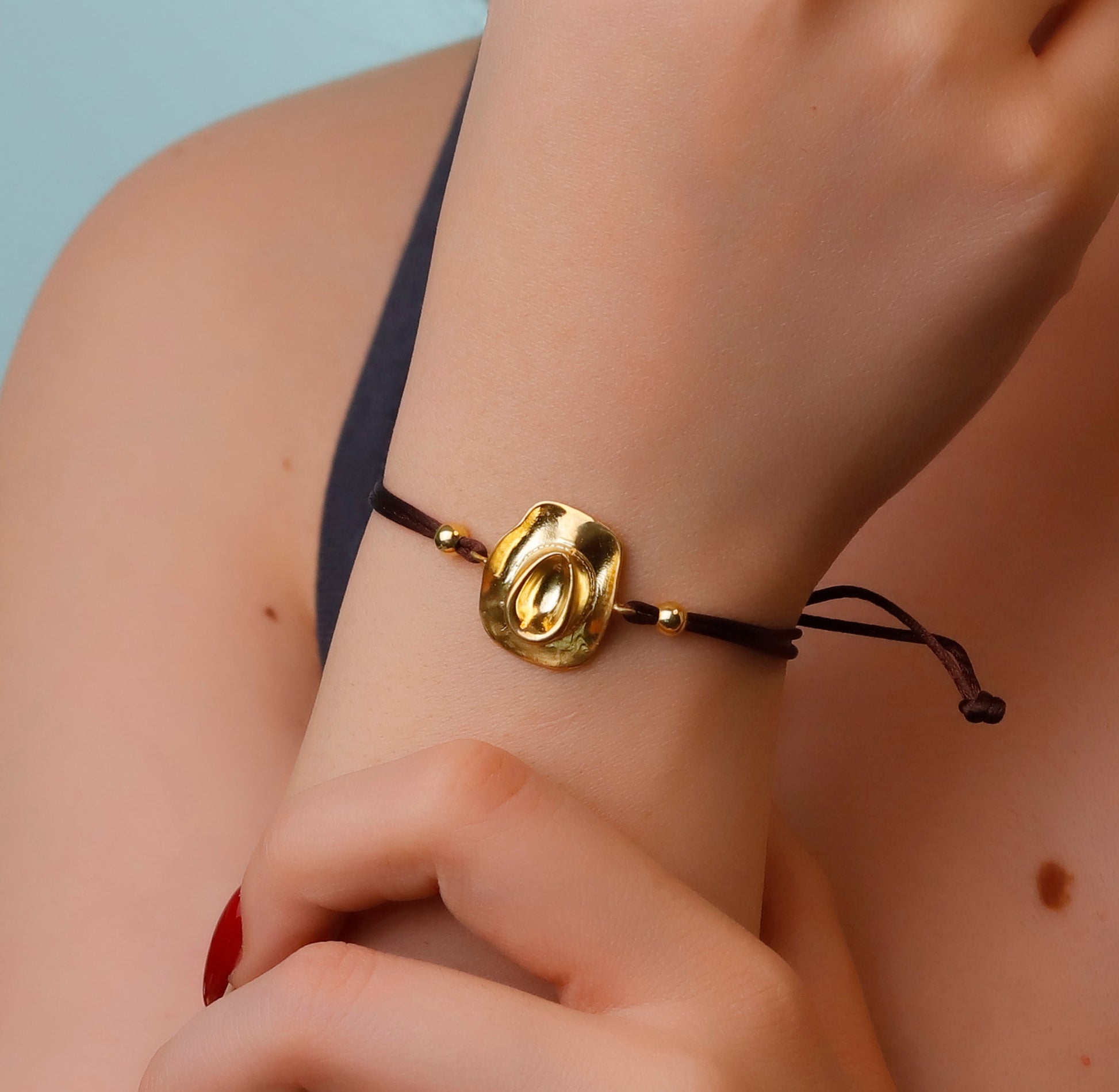 Gold bracelet with a black cord on a wrist against a neutral background
