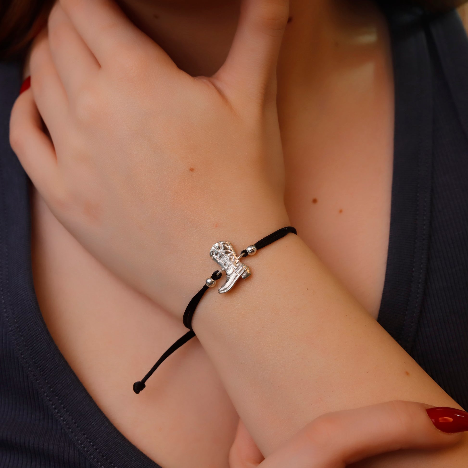 Close-up of a wrist wearing a black bracelet with a silver charm, held by a person with red nail polish.