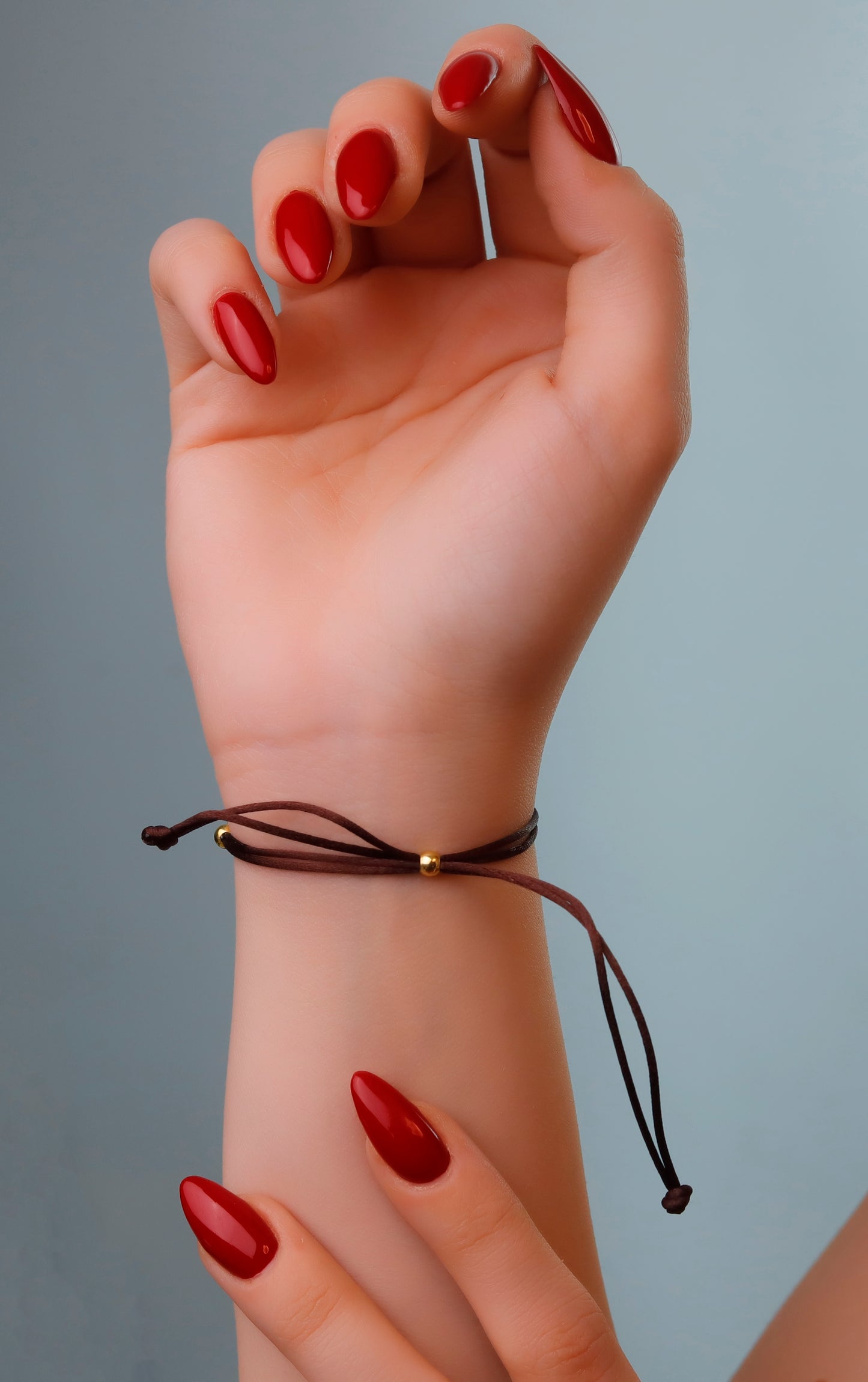 Hand with red nail polish wearing a brown bracelet on a gray background
