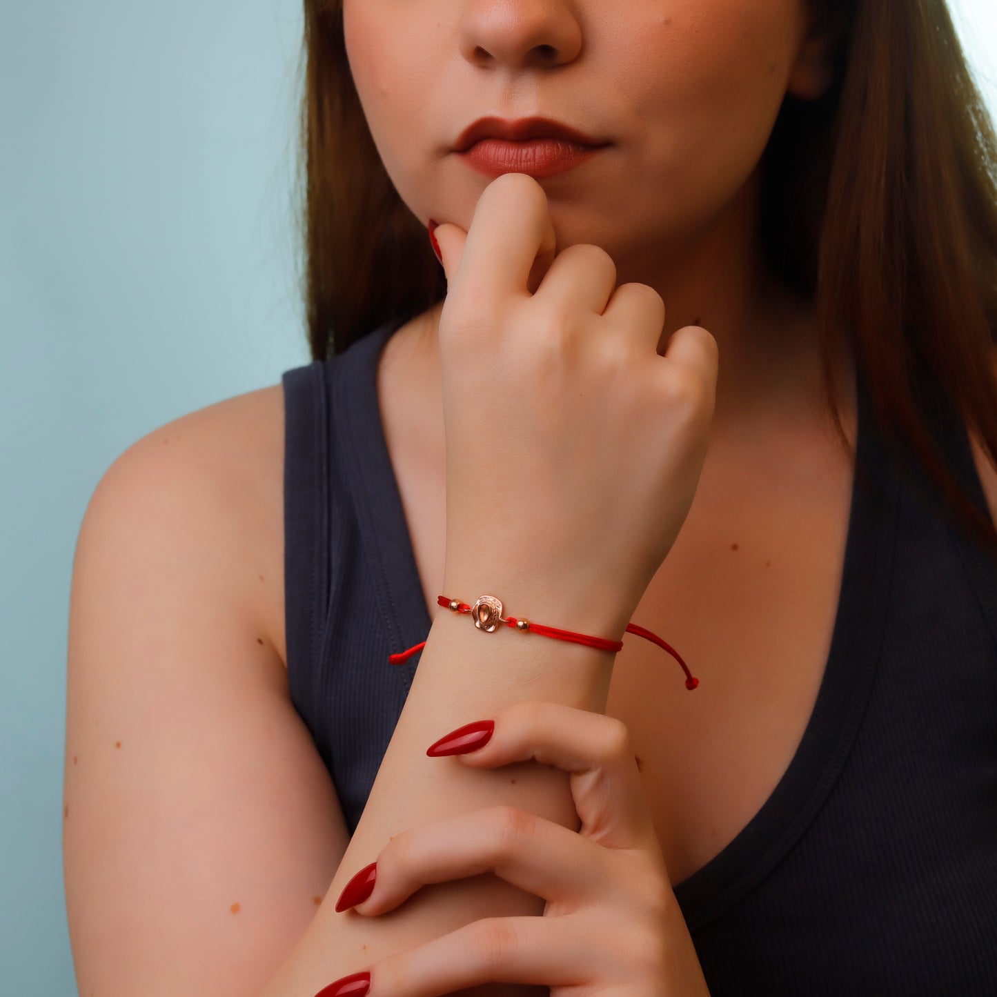 Woman wearing a red bracelet with a small gold charm, against a light blue background
