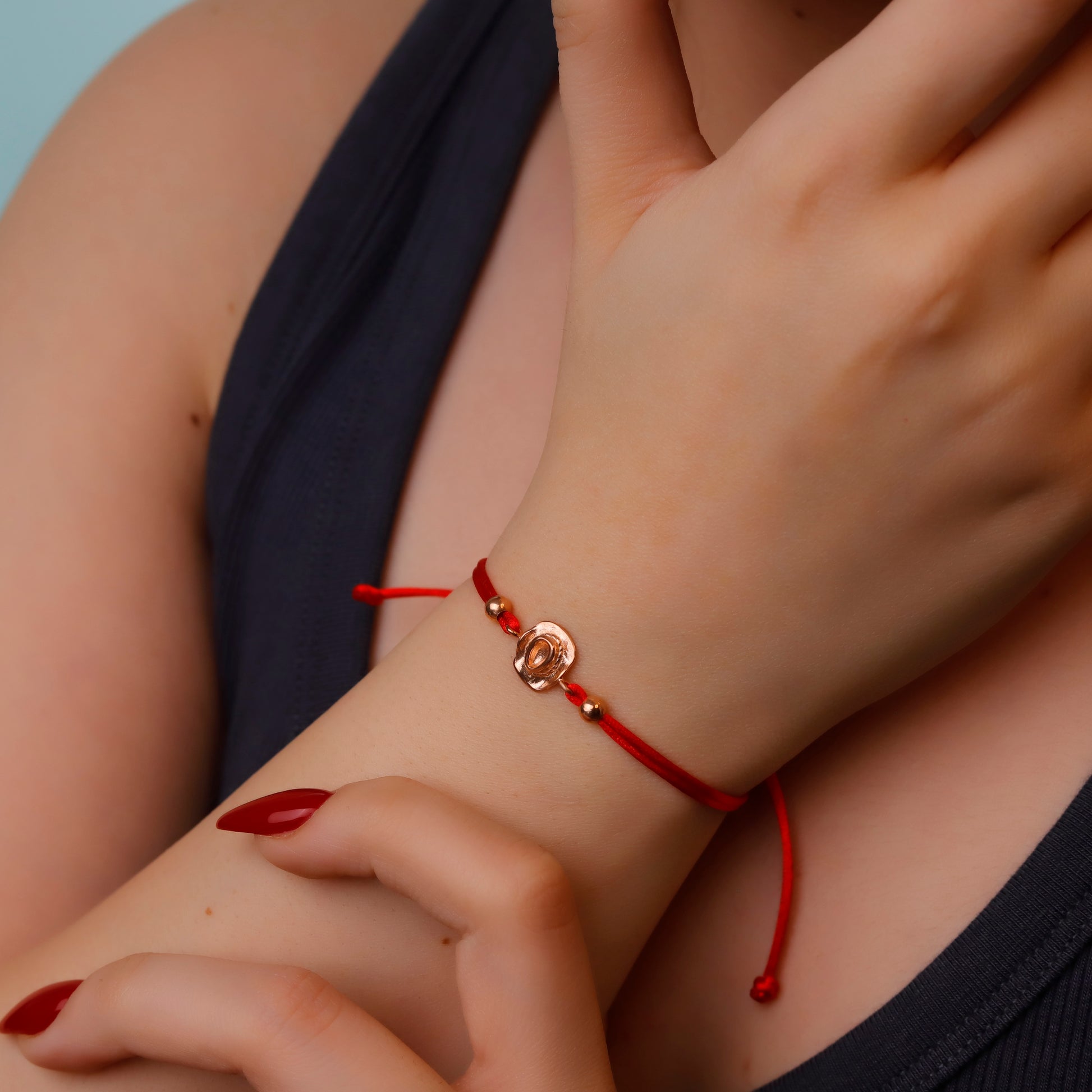 Close-up of a wrist wearing a red string bracelet with a heart charm.