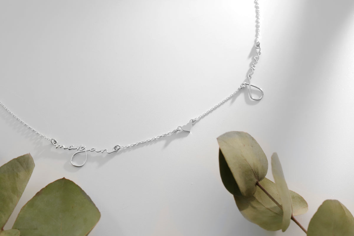 Silver necklace with a delicate chain on a white background with green leaves.