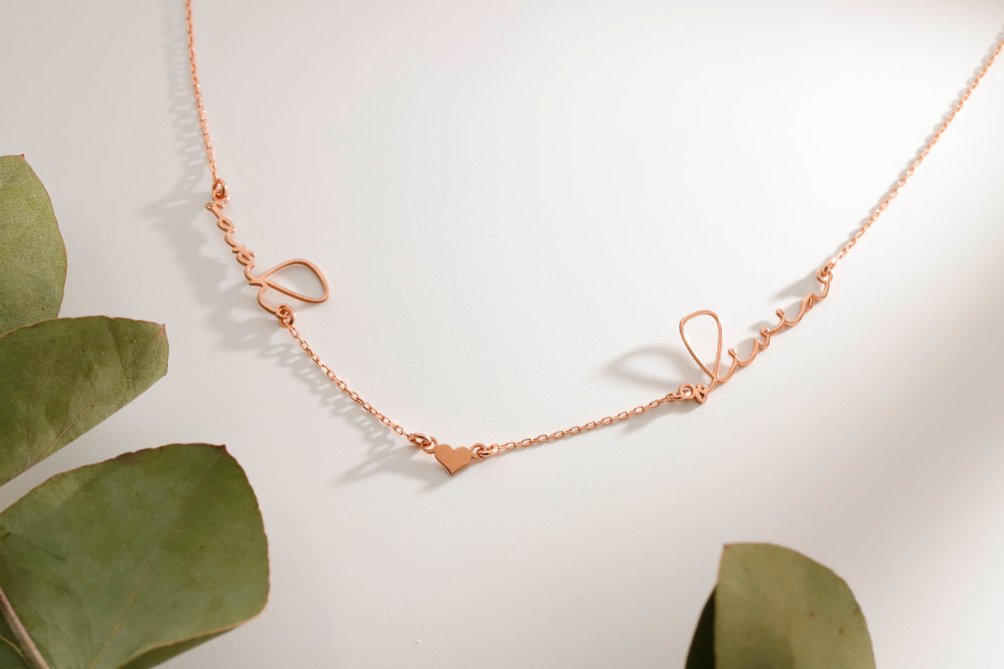 Rose gold necklace on a light background with green leaves