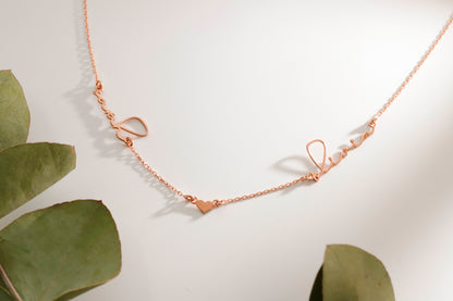 Rose gold necklace on a light background with green leaves