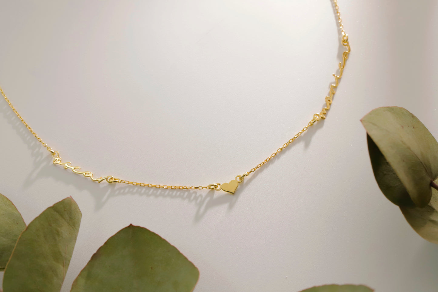Gold necklace on a white background with green leaves
