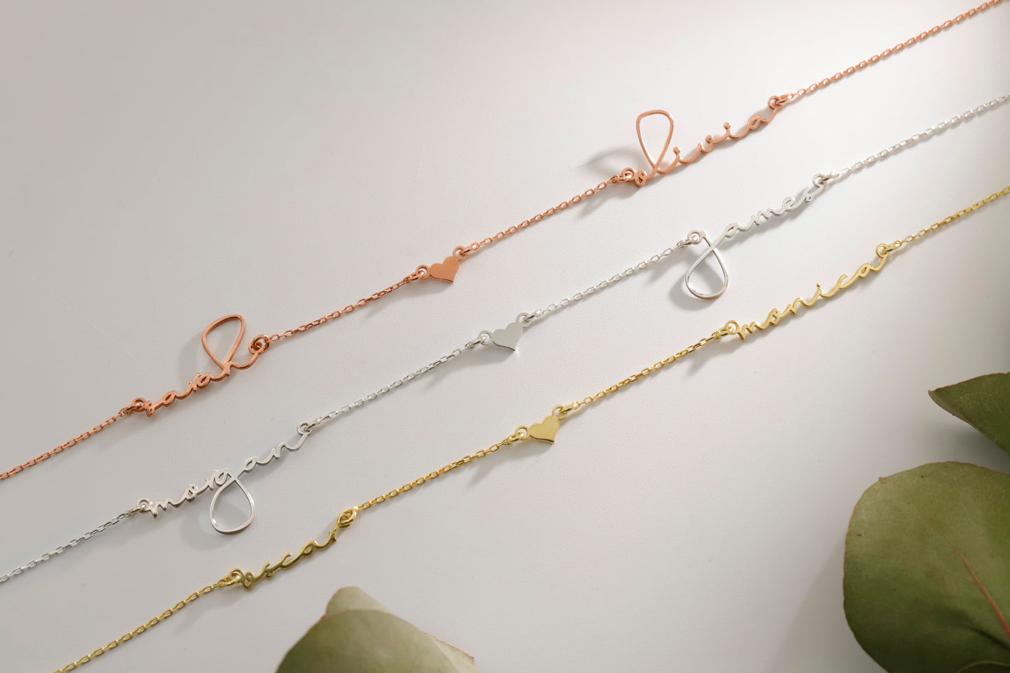 Three gold necklaces on a light gray background with green leaves.