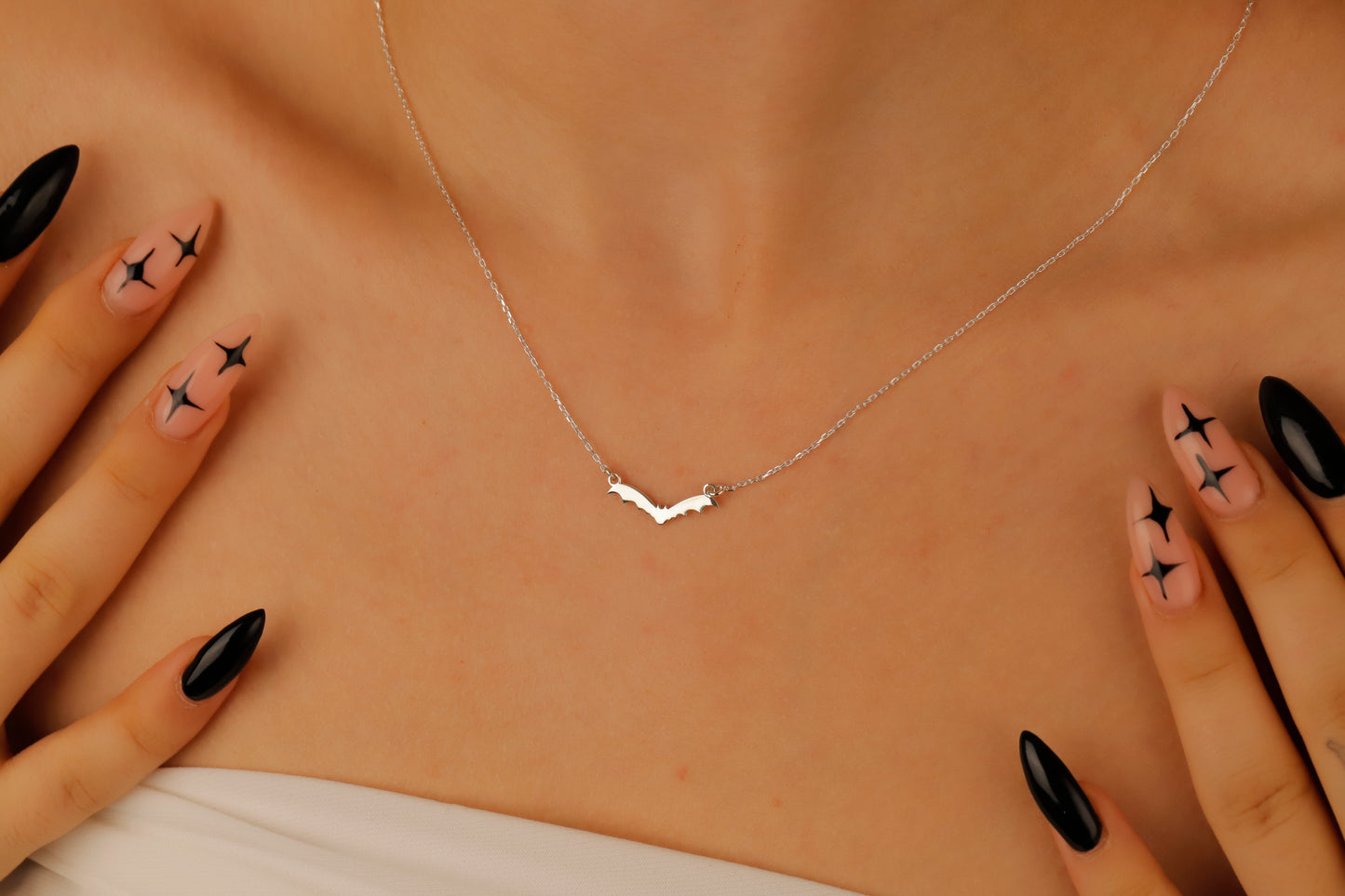 Silver necklace on a person's neck with hands touching the sides, against a beige background.