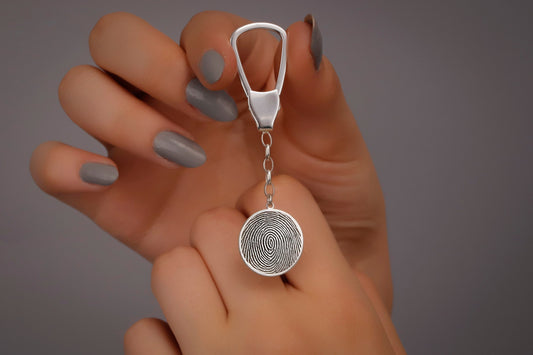 A sterling silver keychain with a fingerprint-like pattern on it, held between fingers with a neutral background.