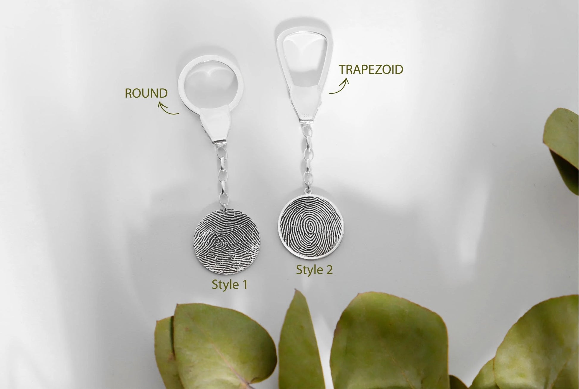 Two silver fingerprint keychains labeled 'Round' and 'Trapezoid' with green leaves in the background.