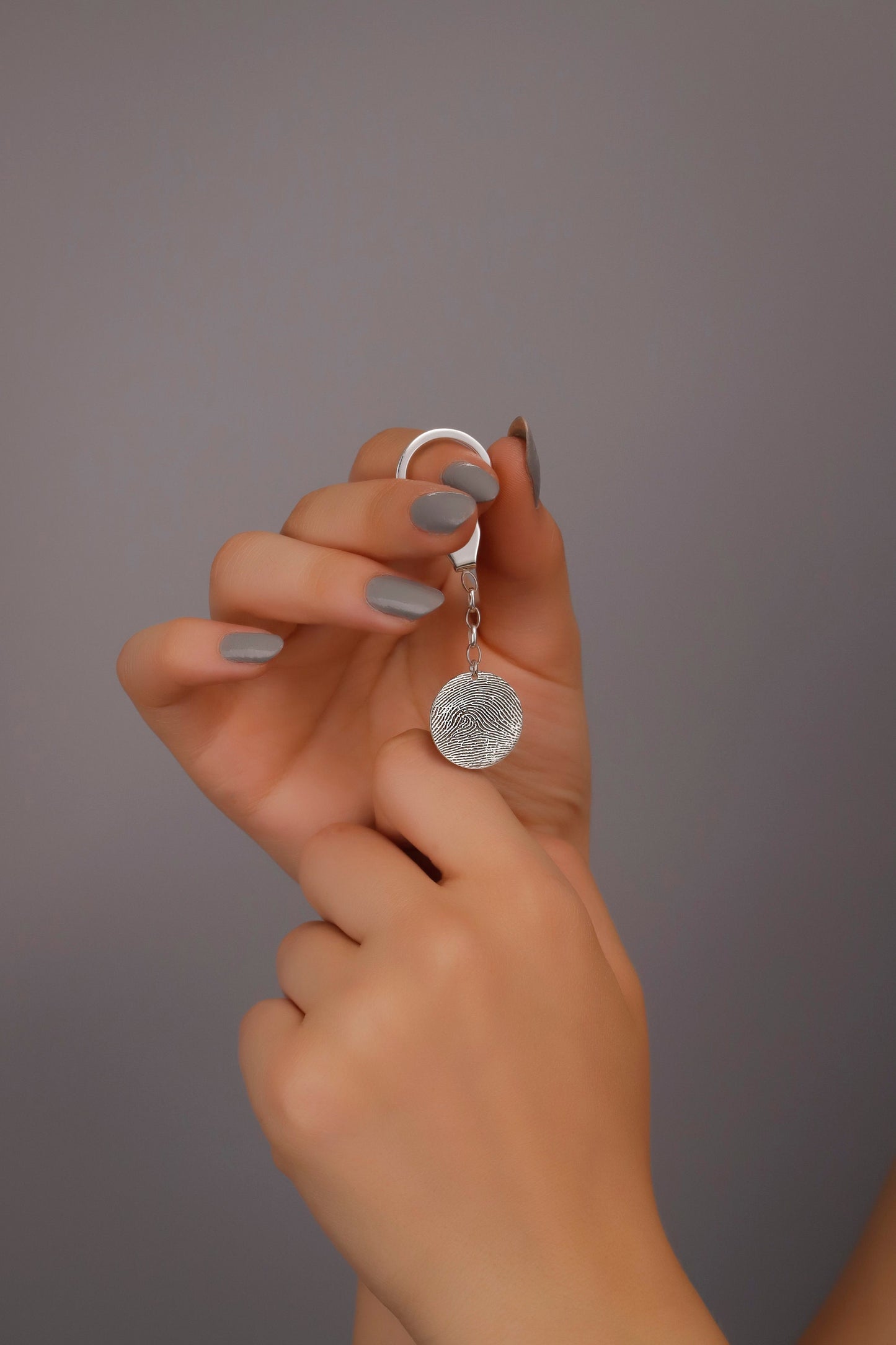 A sterling silver keychain with a fingerprint-like pattern on it, held between fingers with a neutral background.