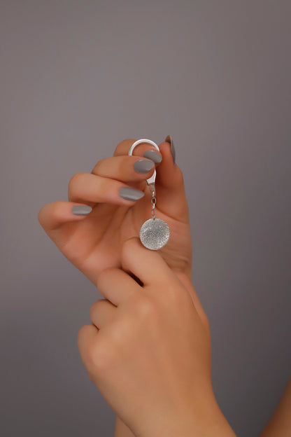 A sterling silver keychain with a fingerprint-like pattern on it, held between fingers with a neutral background.