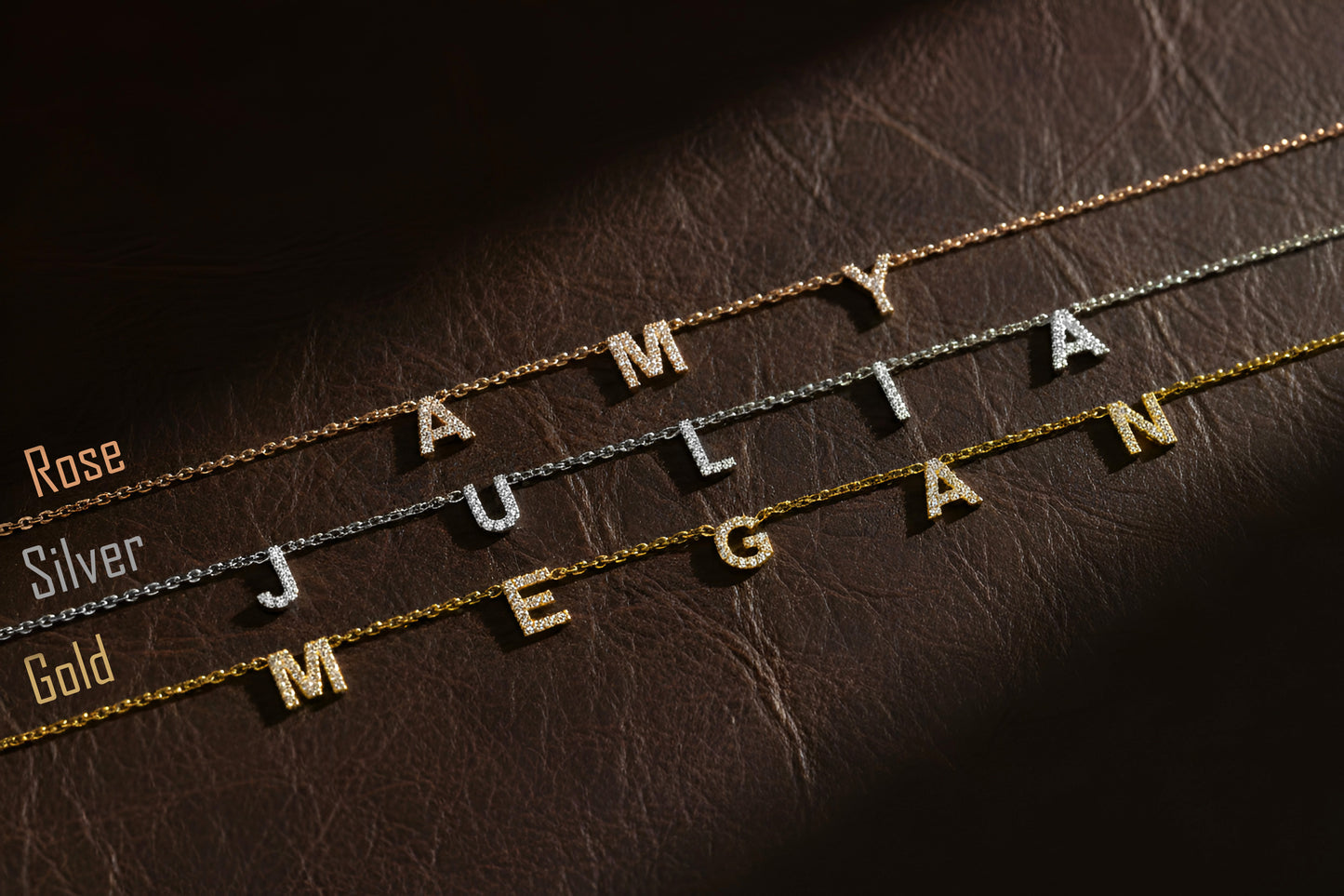 Three gold necklaces with engraved names on a brown leather surface.