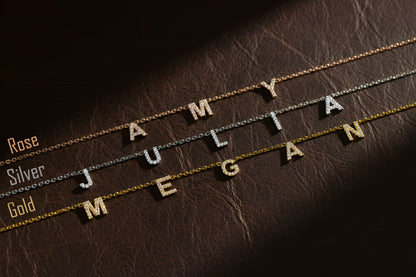 Three gold necklaces with engraved names on a brown leather surface.
