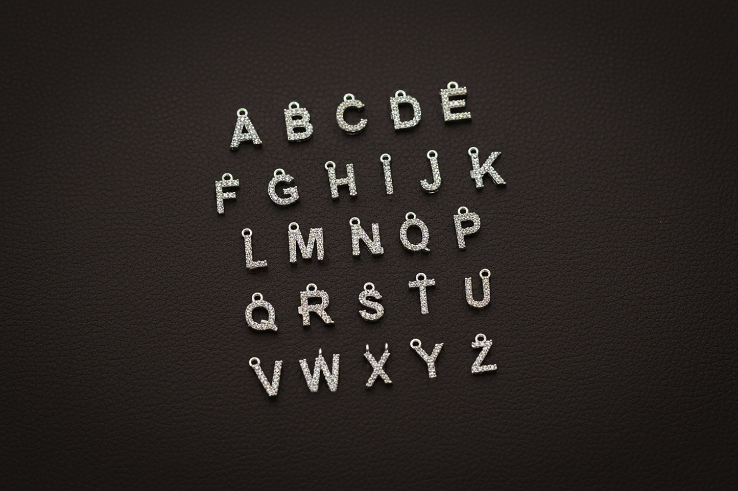 Silver letter charms arranged in alphabetical order on a black background