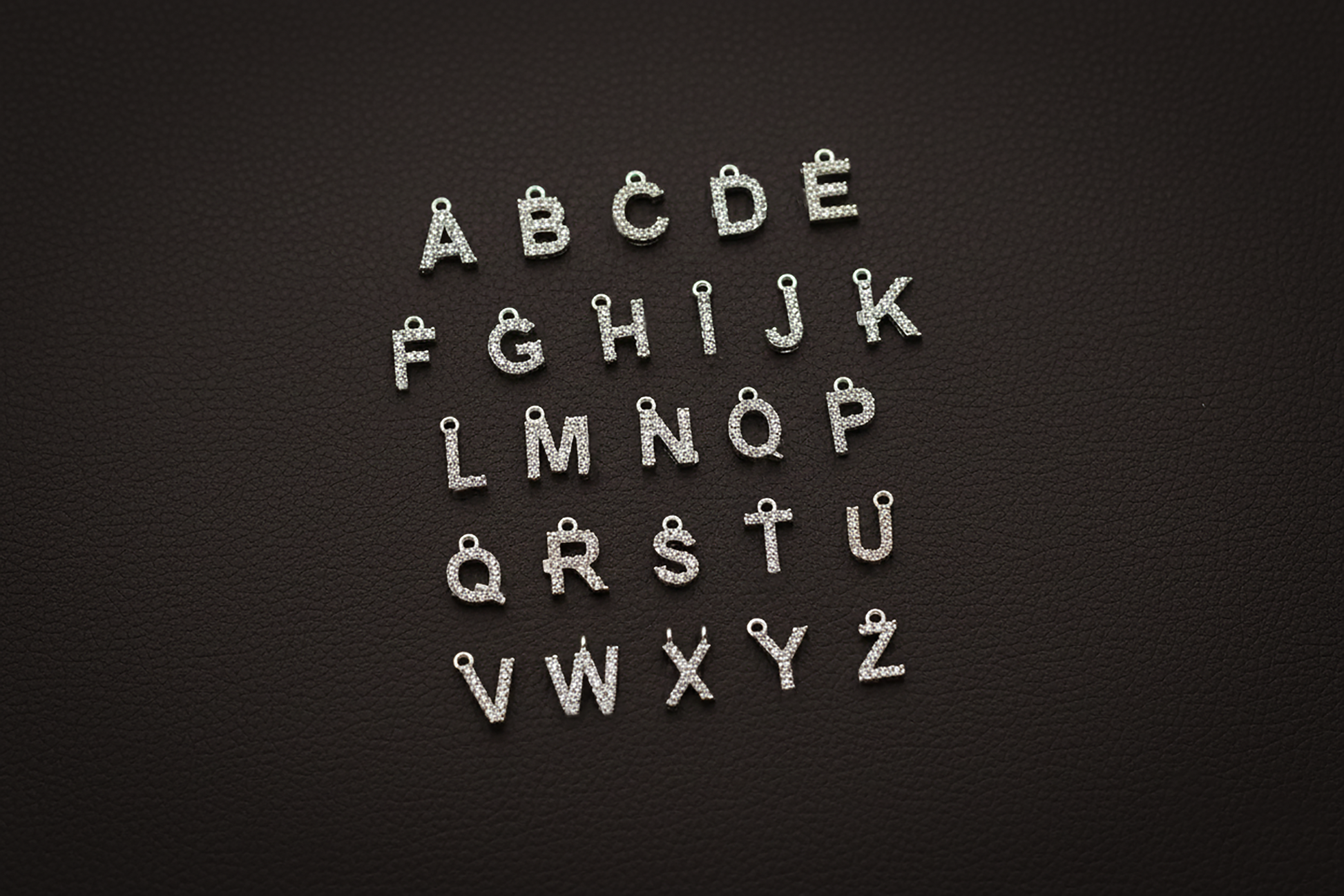 Silver letter charms arranged in alphabetical order on a black background