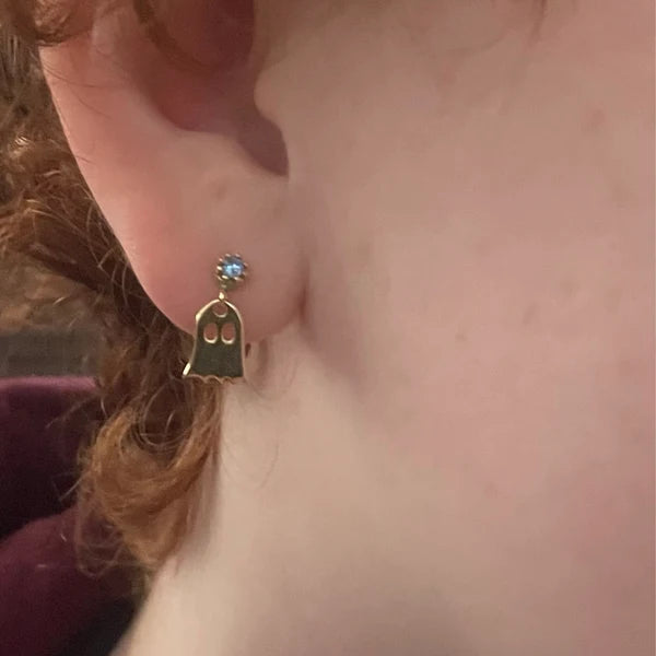 Gold ghost-shaped earring worn on an ear with a blurred background