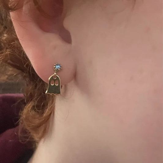 Gold ghost-shaped earring worn on an ear with a blurred background