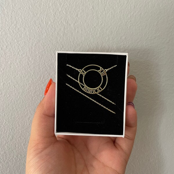 Hand holding a box with a necklace inside against a plain background