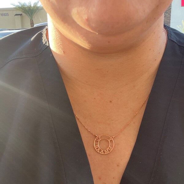 Person wearing a gold necklace with a circular pendant featuring Roman numerals.