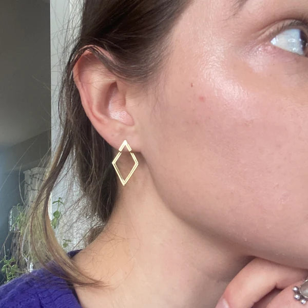 Close-up of a person wearing a gold geometric hoop earring.