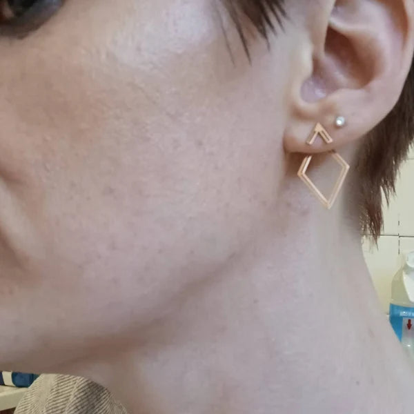 Close-up of an ear wearing a gold geometric earring with a blurred background.