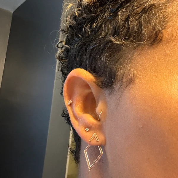 Close-up of an ear with gold earrings against a neutral background