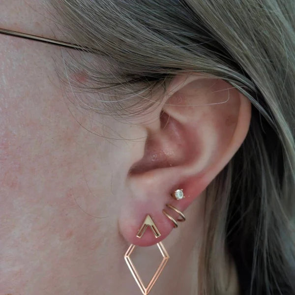 Close-up of an ear wearing gold geometric earrings with a blurred background