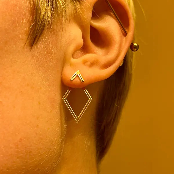 Close-up of an ear wearing a gold geometric earring against a warm-toned background
