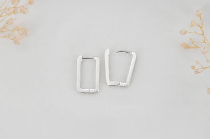 A close-up image of a woman's ear wearing a sterling silver rectangle link huggie hoop earring.