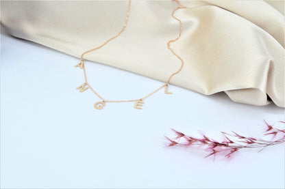 Gold necklace with letter pendants on a beige fabric background