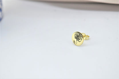 A close-up image of  a small gold-colored floral earring.