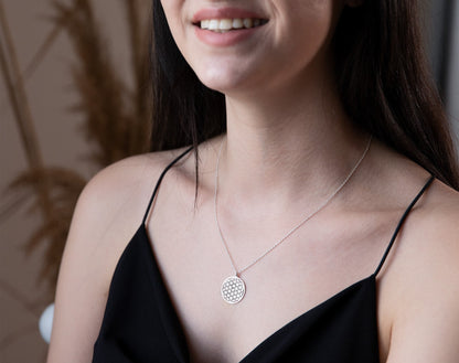 Woman wearing a silver necklace with a circular pendant against a blurred background