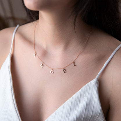 Necklace with 'ANGEL' letters worn by a person in a white top