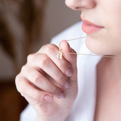 A close-up image of a woman wearing a sterling silver necklace with a gothic style initial pendant.