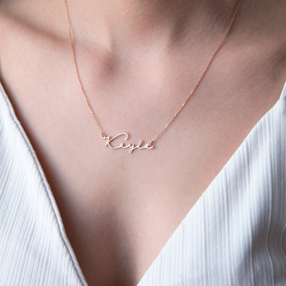 A sterling silver necklace with the name 'Katie' inscribed on it, worn by a person with a blurred background.