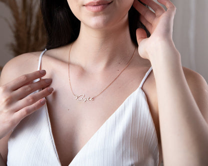 A sterling silver necklace with the name 'Katie' inscribed on it, worn by a person with a blurred background.