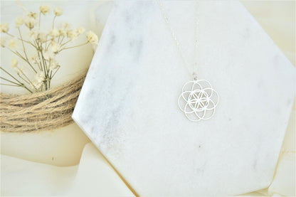 a silver pendant necklace with a floral seed of life design.