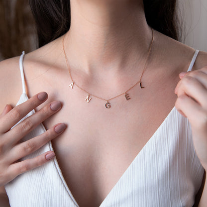 Necklace with letter pendants worn by a person in a white top