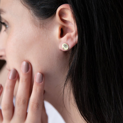 A close-up image of a woman's face with a small gold-colored floral earring in her ear.