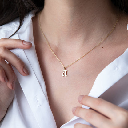 A close-up image of a woman wearing a sterling silver necklace with a gothic style initial pendant.
