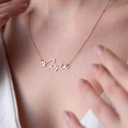 A sterling silver necklace with the name 'Katie' inscribed on it, worn by a person with a blurred background.
