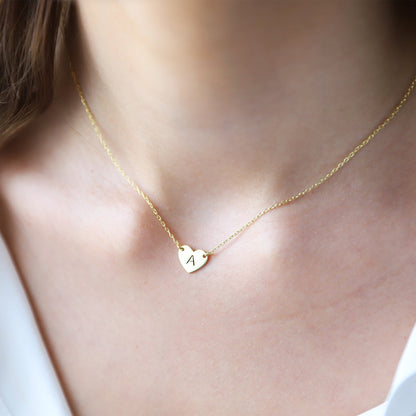 Gold necklace with a heart-shaped pendant featuring the letter 'A' on a blurred background