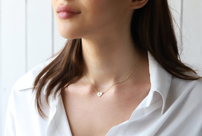 Woman wearing a delicate gold necklace with a heart pendant against a white background