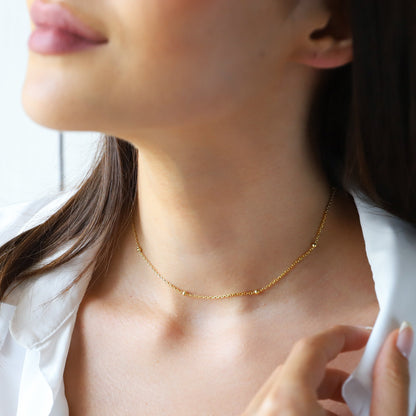 A woman wearing a gold beaded chain necklace with a subtle golden hue.